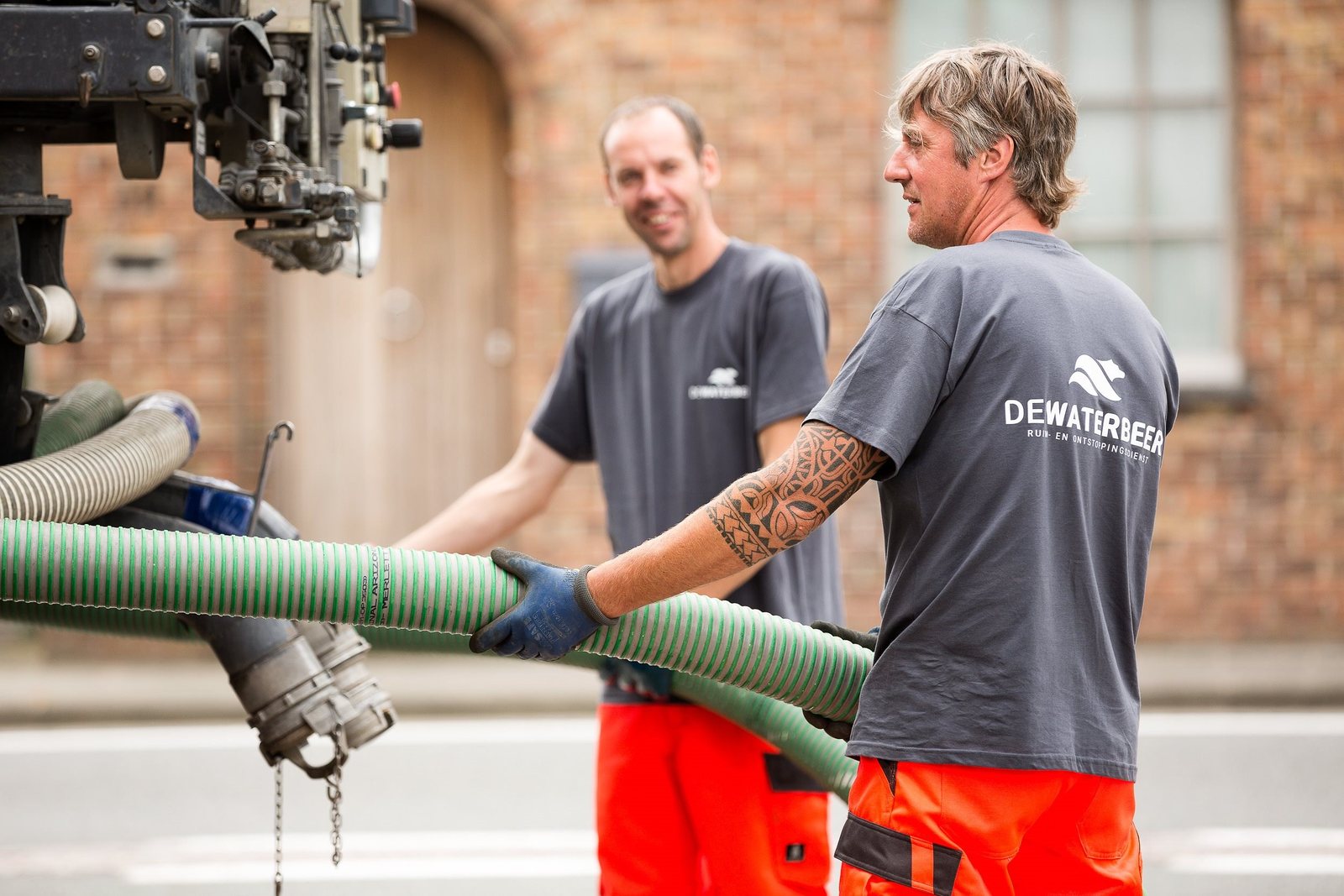 Twee vakmannen met een ruimslang in de straat